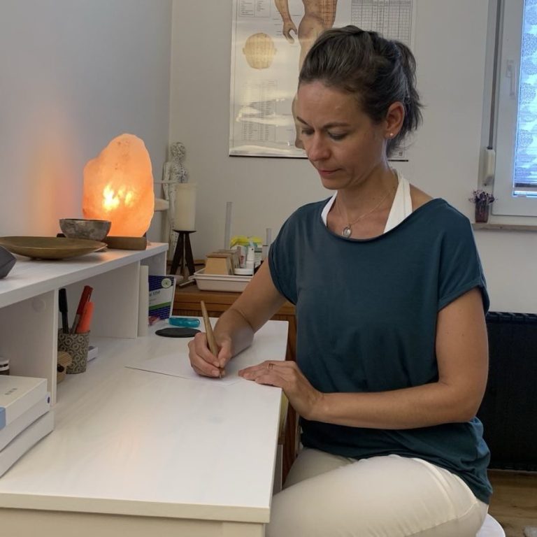 Heilpraktikerin Stephanie Bönisch schreibt an ihrem Schreibtisch in der Praxis