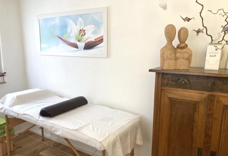 Behandlungsraum mit Massagetisch, Dekoration und Holzelementen.