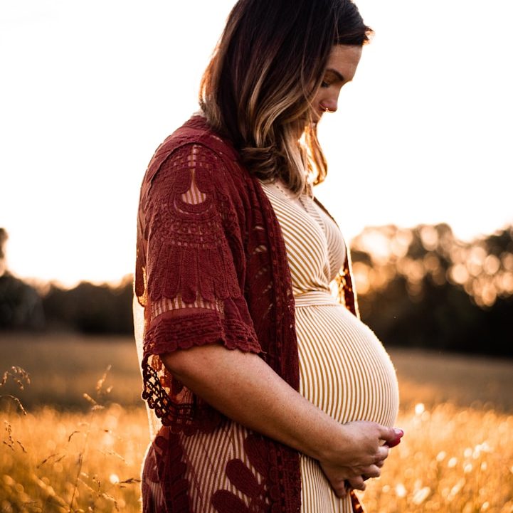 Schwangere hält ihren Babybauch vor dem Hintergrund eines Getreidefeldes